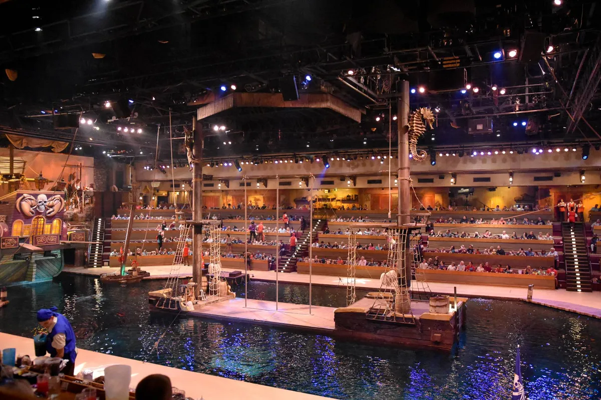 An interior shot of a vibrant, themed venue hosting a live water-based performance, with visible stage, audience seating, and immersive decor. The bustling atmosphere highlights entertainment and dining experiences similar to those offered in the Xplorie perks.