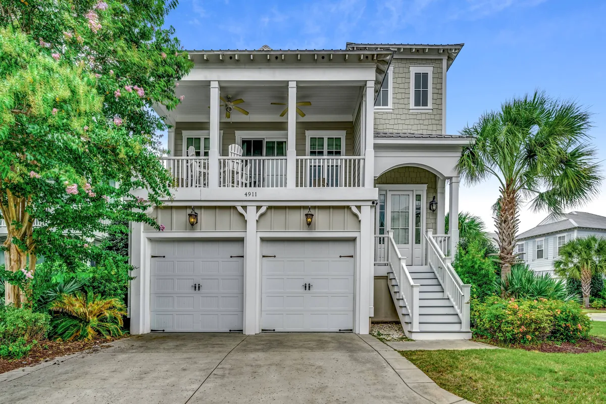 This image showcases the inviting exterior of a spacious single-family home in North Myrtle Beach, featuring a charming front porch, a scenic balcony perfect for sunset views, and meticulously landscaped gardens. The warm lighting and welcoming facade set a relaxing, coastal mood ideal for vacationers.