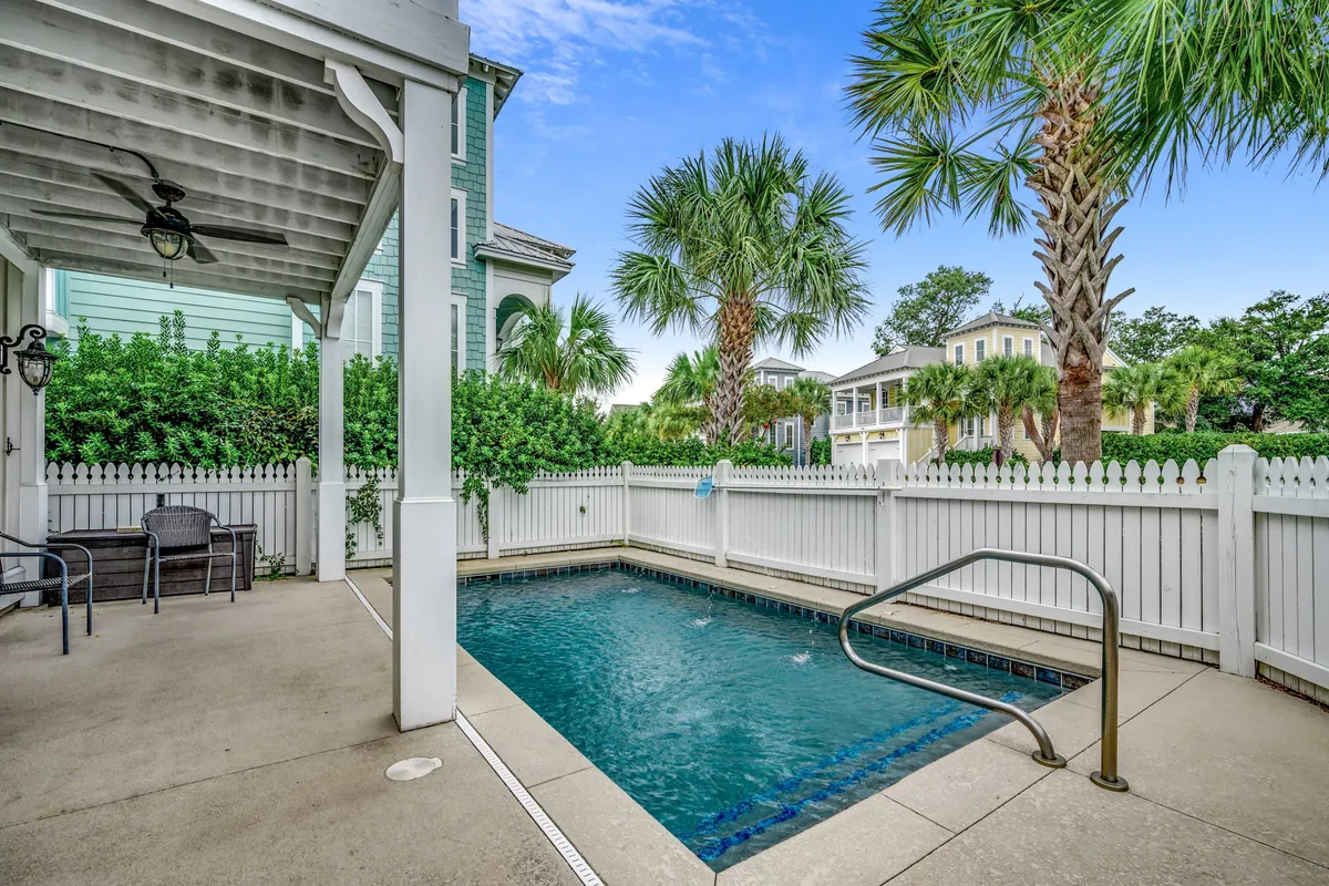 A sparkling blue pool is bordered by lush palm trees and comfortable patio furniture, creating a relaxing and inviting atmosphere. The well-maintained pool area looks perfect for swimming, sunbathing, or simply lounging with friends and family.
