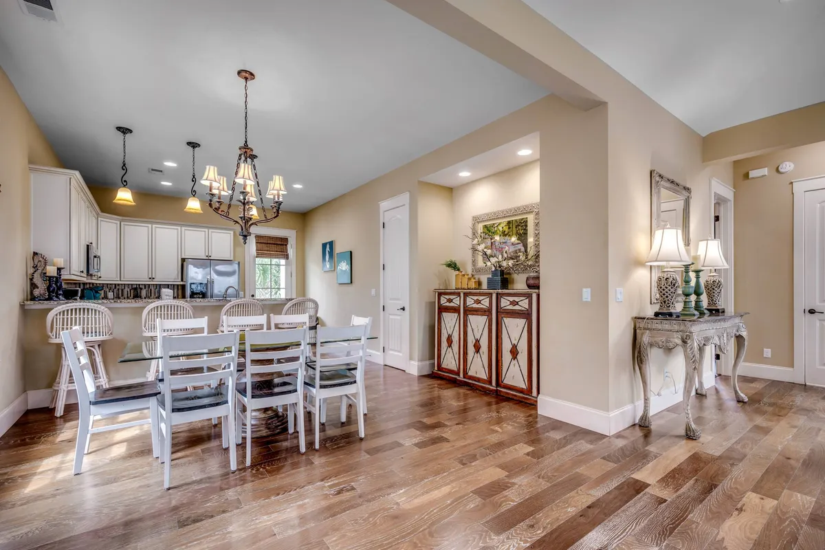 A stylish dining area with a large table under a decorative chandelier, seamlessly opening to the adjacent kitchen area. The console table and decor create a warm, inviting mood ideal for both family meals and entertaining guests.