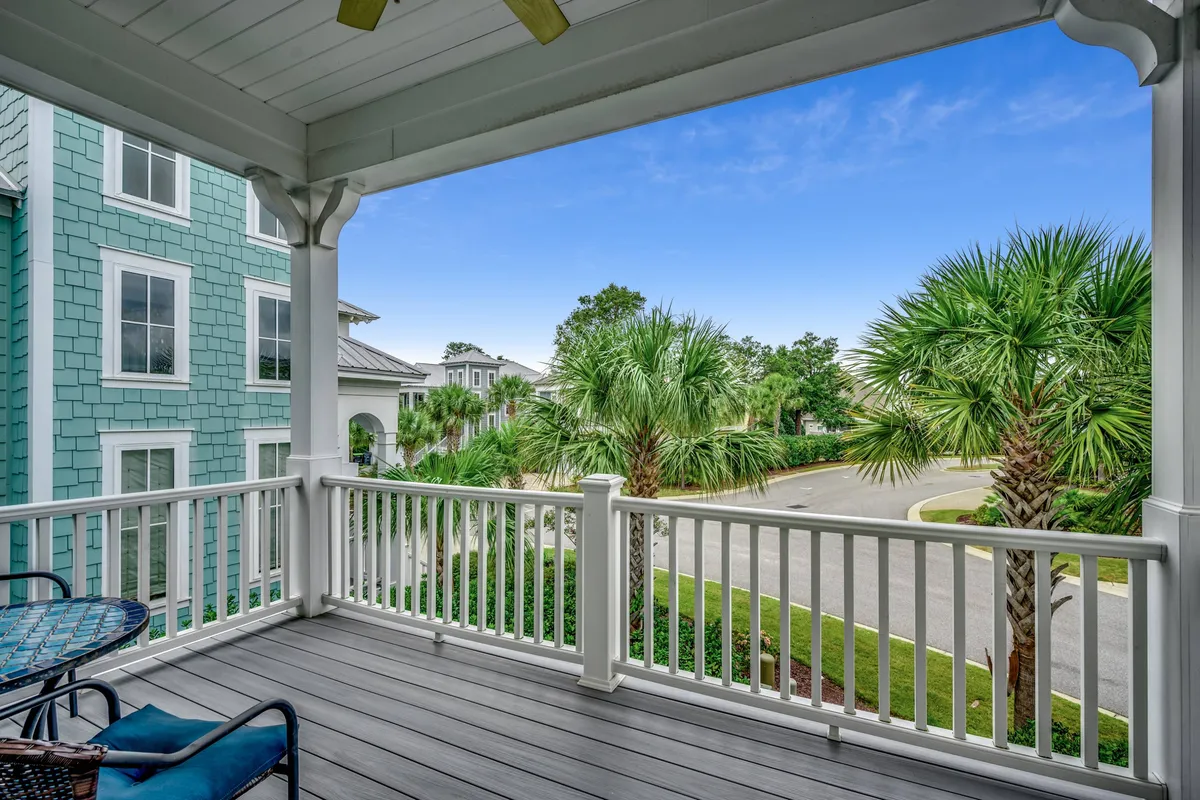 A serene second-floor balcony with a railing overlooks palm trees and a quiet street, featuring inviting outdoor furniture. The space feels perfect for morning coffee, reading, or unwinding above it all.